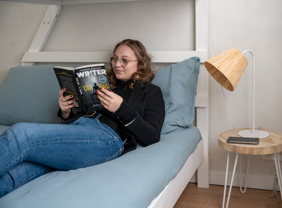Gast leest een boek op het onderste bed van het stapelbed